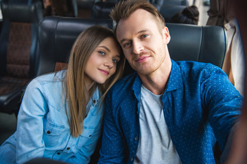 Wall Mural - cheerful man taking selfie with young girlfriend during trip on travel bus