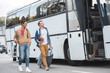 © LIGHTFIELD STUDIOS - selective focus of man with rugby ball carrying wheeled bag while his mixed race male friend walking near travel bus at street