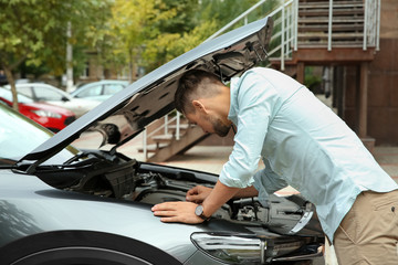 Man fixing broken car on city street