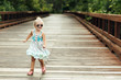 © Samantha McBride - Smiling blond girl wearing sunglasses walking on wooden bridge