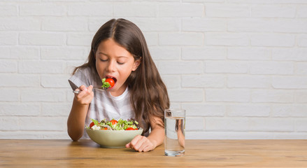 Poster - Young hispanic kid sitting on the table eating healthy salad with a confident expression on smart face thinking serious