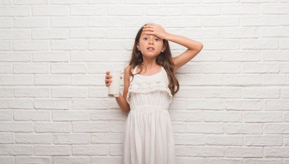 Poster - Young hispanic kid over white brick wall drinking a glass of milk stressed with hand on head, shocked with shame and surprise face, angry and frustrated. Fear and upset for mistake.