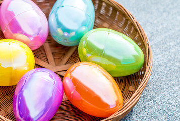 Plastic Easter eggs sitting in a circular brown basket on a texture.d background