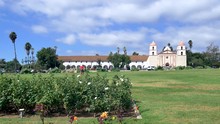 Reveal Shot Of The Picturesque Santa Barbara Mission Building From Behind A Bright Colorful Orange Rose In California.