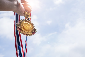 Winner hand raised holding gold medals with Thai ribbon against blue sky. Golden medals is award for highest achievement for sport or business. Success Awards concept