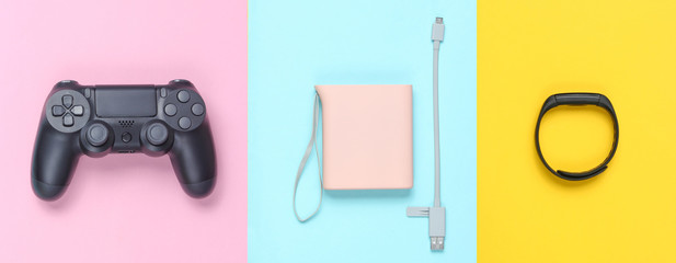 Power bank and usb cable, gamepad, smart bracelet on colored pastel background. Modern gadgets. Top view, minimalism..