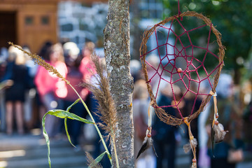 Wall Mural - Small dreamcatcher is hanging in a tree in front of a crowd waiting to enter in the church as part of a native arts festival - 2/2 - Closeup picture with blurry people in the background