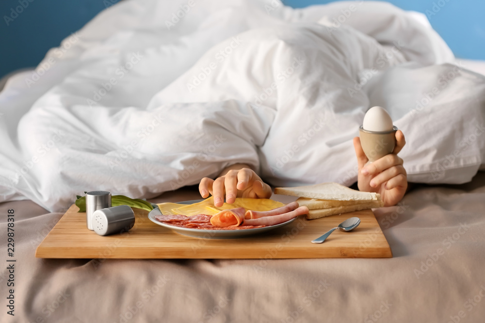 Sleepy woman under blanket with delicious breakfast on bed