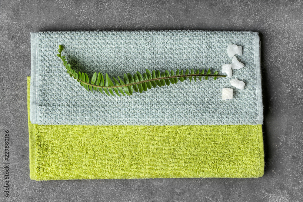 Folded clean towels with green leaf on grey background, top view