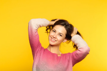 Wall Mural - happy joyful smiling girl making pig tails from her hair. relaxed carefree teenage lifestyle and childish behavior. young beautiful brown haired woman portrait on yellow background.