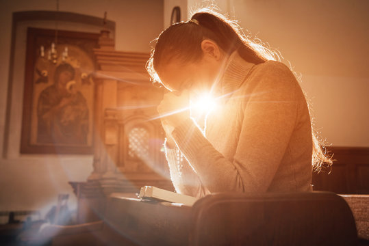 christian woman praying in church. hands crossed and holy bible on wooden desk.
