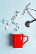 Red mug with sugar cubes, blue ribbon and stethoscope on a blue background.