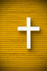 white christian cross on a yellow wooden wall with vignetting