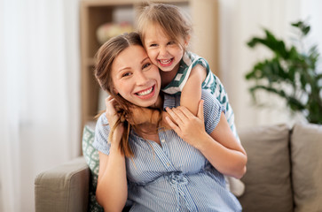 Wall Mural - pregnancy, people and family concept - happy pregnant mother and little daughter hugging at home