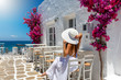 Frau in weißem Kleid sitzt vor einer typisch griechischen Kullise mit weißen Häusern und bunten Blumen auf den Kykladen
