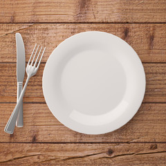 Fototapete - Top view of ceramic plate with fork and knife on wooden table. 3d 