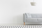 Fototapeta  - Lamp above grey couch in white minimal apartment interior with copy space on empty wall. Real photo