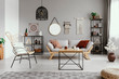 Mirror, macrame and graphic on the grey wall of warm ethno living room with stylish furniture and cozy patterned carpet