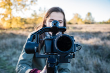 Female Videographer Holding A Gimbal With Mirrorless Camera. Woman With Stabilized Camera Rig Filming Outdoors On A Sunny Afternoon