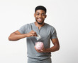 Smiling african-american man putting money in his piggy bank