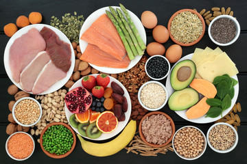 Wall Mural - Super food for body builders high in protein including meat, fish, dairy, multi vitamin and fish oil tablets, legumes, fruit, cereals, vegetables, herbs, nuts and seeds on dark wood background.