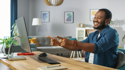 Wall Mural - Portrait of the Handsome African American Man Pointing at the Screen with Two Fingers while Sitting at His Workplace. Young Man Having Fun at Home.