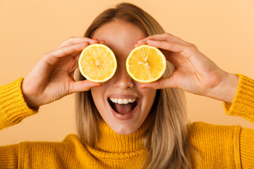 Poster - Beautiful woman covering eyes with citrus lemons posing isolated over yellow wall background.