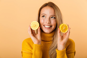 Sticker - Beautiful woman holding citrus lemons posing isolated over yellow wall background.