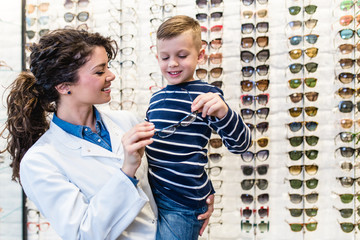 Poster - Ophthalmologist choosing eye frame for a little boy in optical store.