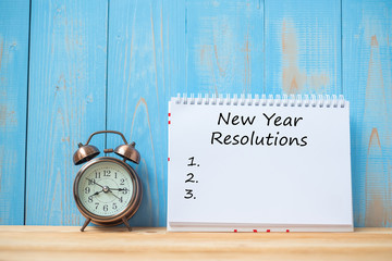 New years Resolutions text on notebook and retro alarm clock  on table and copy space. Goals, Mission and New Start Concept