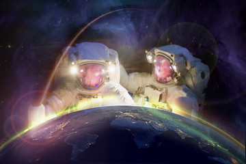 Wall Mural - two huge astronauts look at planet earth from space against the background of the galaxy. elements o