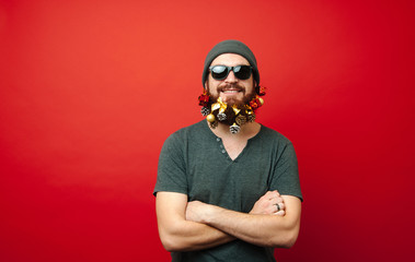 Portrait of cheerful man with decorated beard in christmas toys and looking at the camera with crossed arms