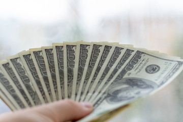 Fan out of 100 dollar bills in male hand. A bunch of money in the male hand. A man holds an unfolded pack of dollars in his hand.