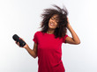 © kohanova1991 - Beautiful african american woman in red t-shirt enjoying and dancing at white background. Modern trendy girl with afro hairstyle listening to music by wireless portable speaker.