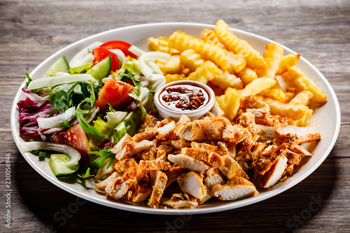 Fototapeta na szkło Kebab - grillowane mięso z frytkami i warzywami na drewnianym tle
