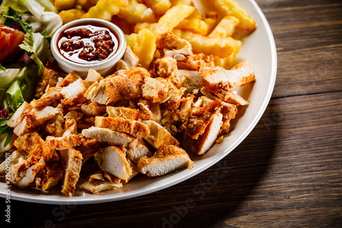 Fototapeta na szkło Kebab - grillowane mięso z frytkami i warzywami na drewnianym tle