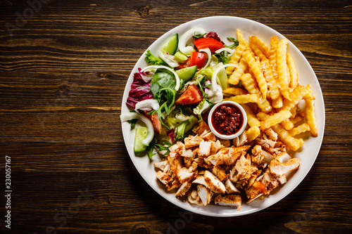 Fototapeta na szkło Kebab - grillowane mięso z frytkami i warzywami na drewnianym tle