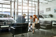 © alfa27 - Sales agent at the table desk telling about car features to cheerful couple of customers at car dealership office