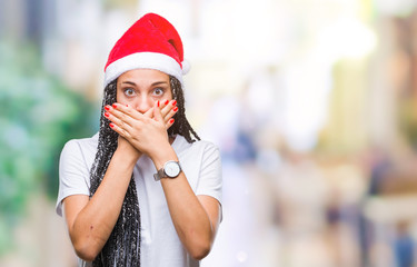 Poster - Young braided hair african american girl wearing christmas hat over isolated background shocked covering mouth with hands for mistake. Secret concept.