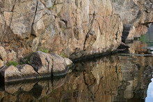 Rock Above The Water Close Up. The Rocky Shore Is Reflected In The Water