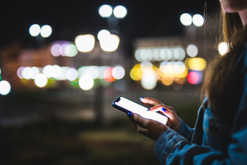 Wall Mural - Woman pointing finger on blank screen smartphone on background bokeh light in night atmospheric city. hipster using in hands clean gadget mobile phone closeup, mockup street, online wifi internet