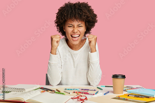 Fotografía Photo of overjoyed African American architect keeps fists clenched, smiles broad
