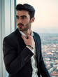 © starsstudio - Portrait of stylish young man wearing business suit, standing next to window overlooking modern European city