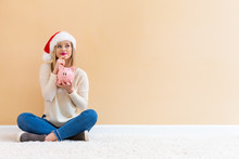 Young Woman With Santa Hat Holding A Piggy Bank On A White Carpet