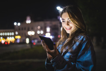 Wall Mural - Young happy woman using tablet outdoors over blurry night city lights