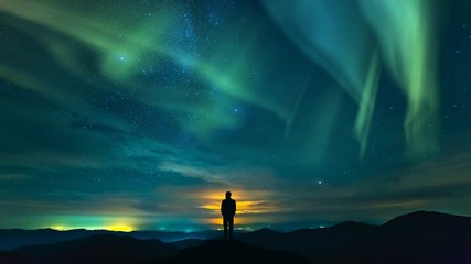 Wall Mural - The man standing on the rock on the starry sky with a northern light background