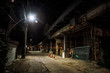 Dark and eerie urban city alley with a vintage railway bridge and construction site at night