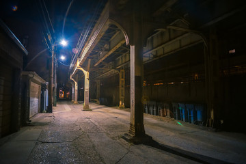 Dark and eerie urban city alley with a vintage railway bridge at night