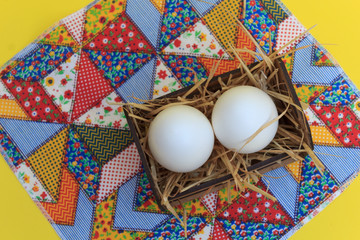 White eggs in a wooden crate, on a patchwork rug, with yellow background.