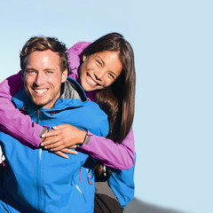 Happy hikers couple active lifestyle hugging laughing outdoors on trek hike. Healthy young people on adventure wearing blue purple jackets. Interracial relationship, Asian woman, Caucasian man.